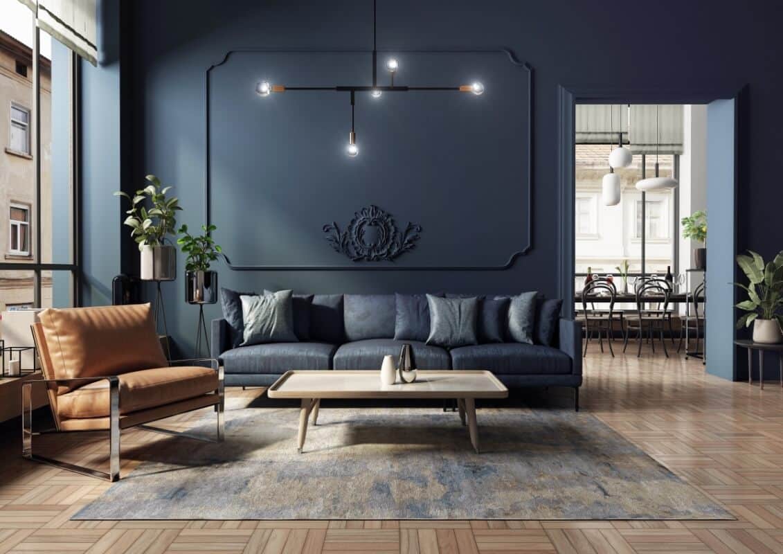 Nowoczesny salon z ciemnoniebieskimi ścianami, wygodną kanapą i eleganckim fotelem w odcieniu brązu. W centrum znajduje się stolik kawowy, a w tle widoczna jadalnia. Wnętrze ozdobione roślinami i stylowym oświetleniem. Idealne miejsce do relaksu z różnorodnymi nogami meblowymi w odmianach!
